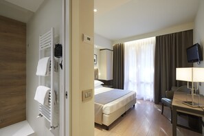 Ein Hotelzimmer mit Bett, Schreibtisch, Fernseher und einem Badezimmer mit Handtuchhalter und Heizkörper.