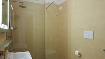 Un baño moderno con ducha de vidrio, lavamanos blanco con espejo, inodoro y bidé.