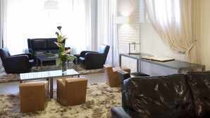 A modern living room with leather furniture, a glass coffee table, and a white brick wall. - Park Hotel Chianti (Barberino Tavarnelle)