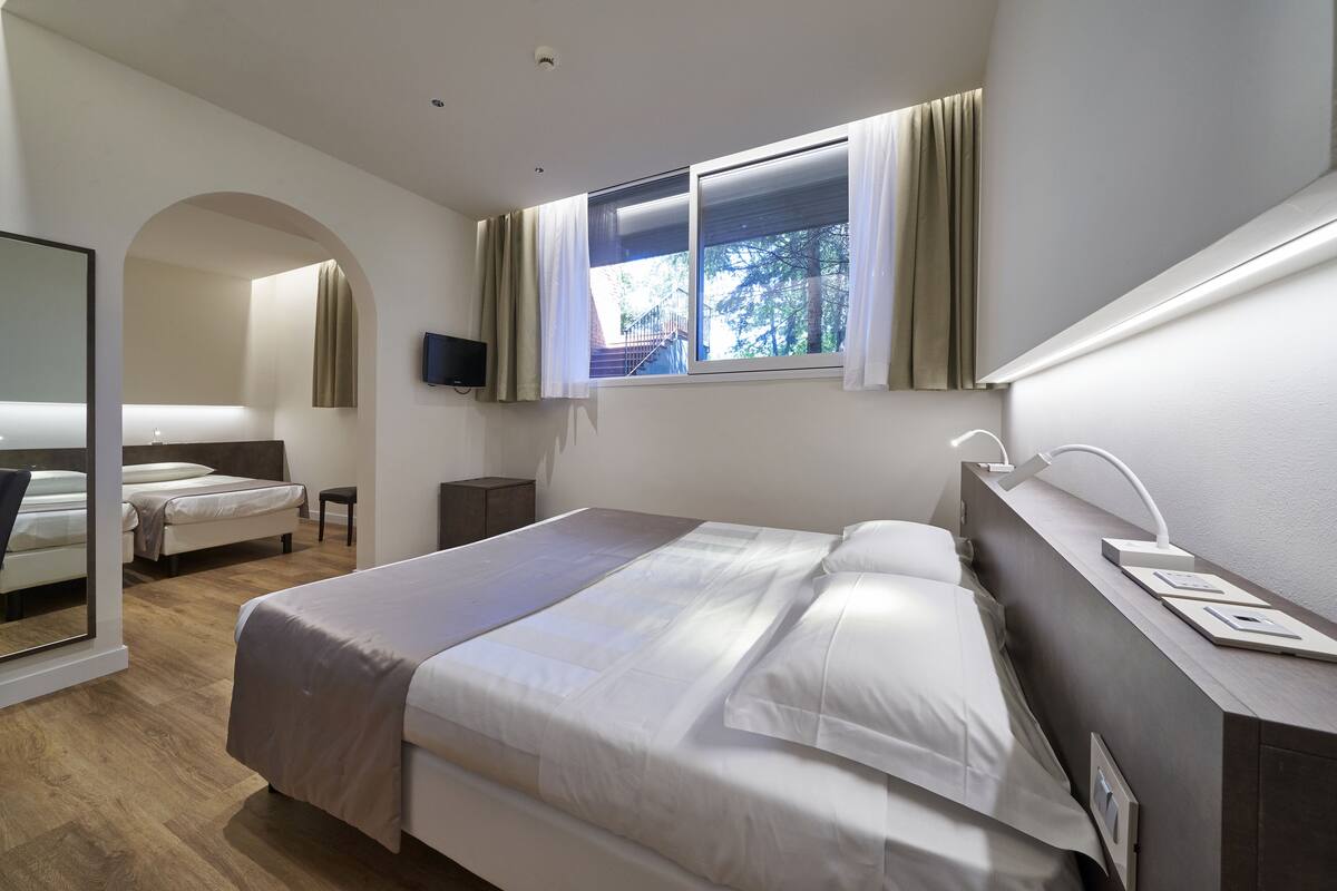 Een moderne hotelkamer met een groot bed, een bureau met lamp, een televisie en een raam met gordijnen.