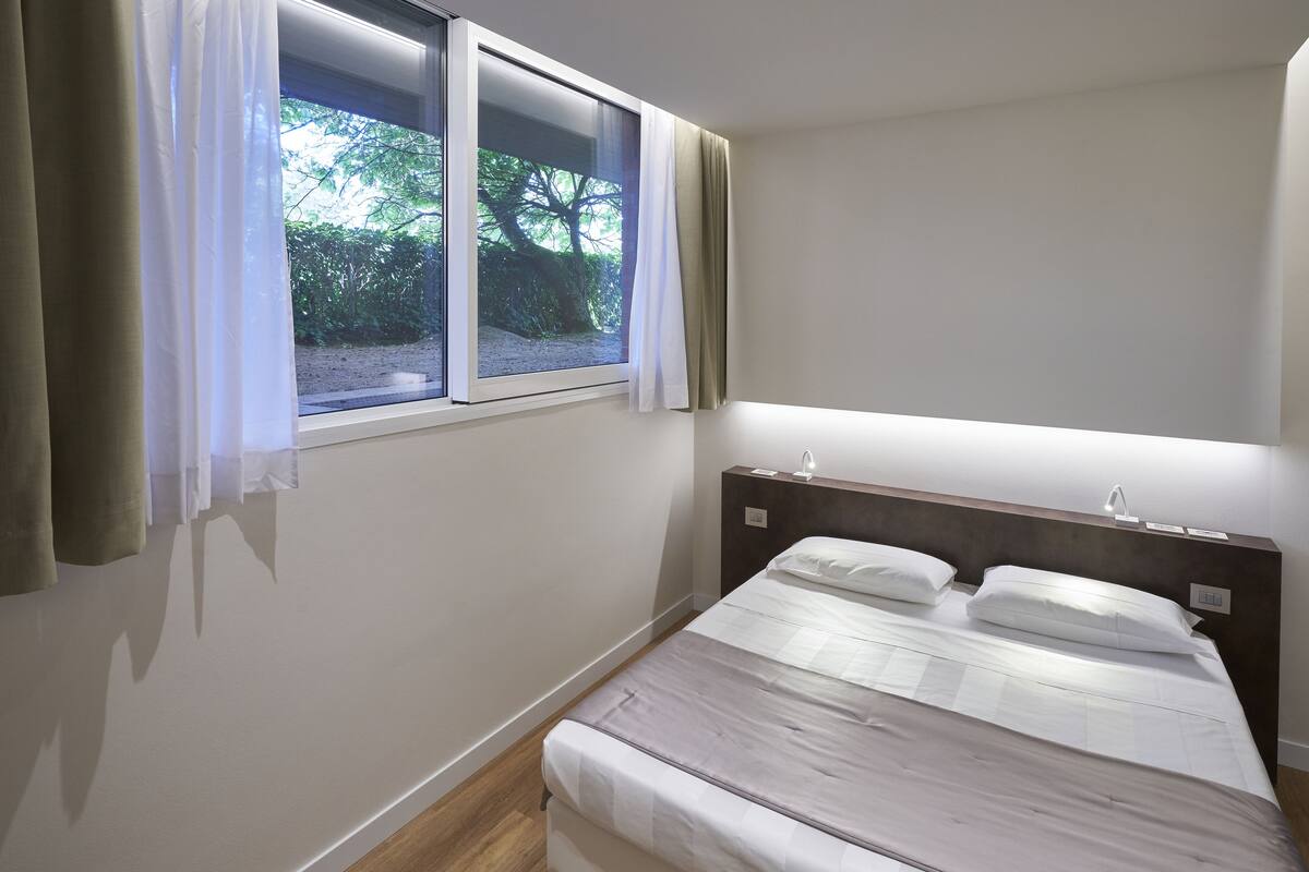 Een slaapkamer met een bed, een raam met gordijnen en een bedlampje.