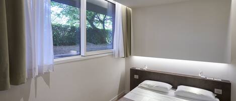 A bedroom with a bed, a window with curtains, and a bedside lamp.