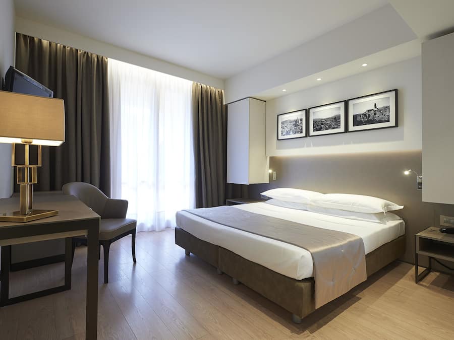 Ein modernes Hotelzimmer mit Bett, Schreibtisch, Stuhl und Fernseher.