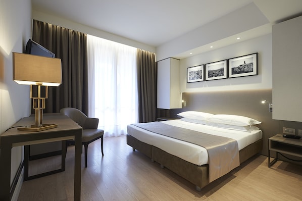 A modern hotel room with a bed, a desk, a chair, and a TV.