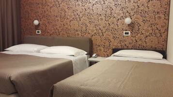 A hotel room with two beds, a nightstand, and a wall with floral wallpaper.