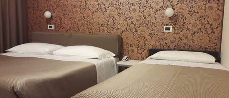 A hotel room with two beds, a nightstand, and a wall with floral wallpaper.