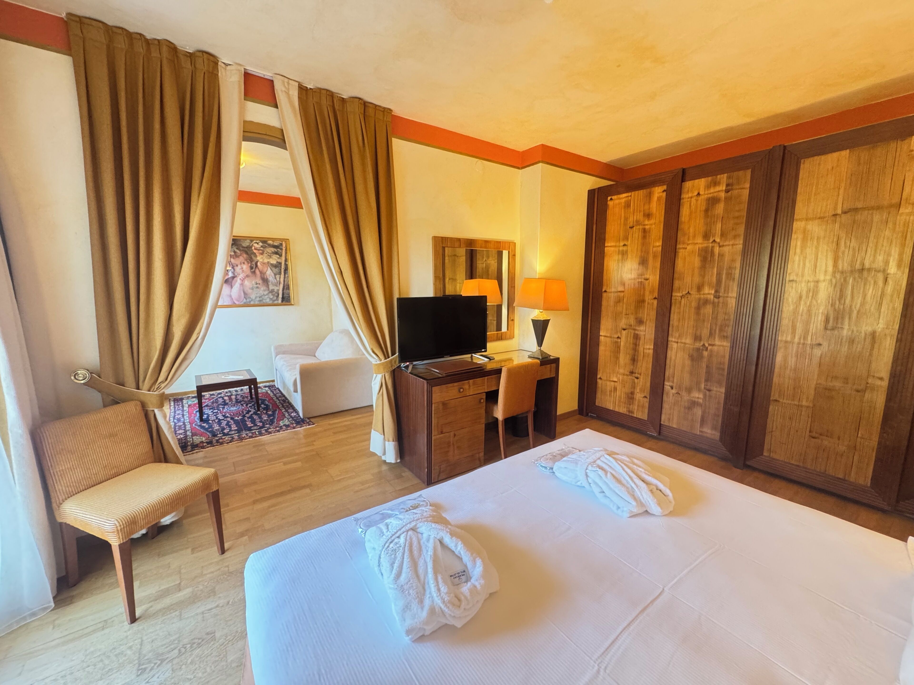 A hotel room with a bed, a desk, a chair, a TV, and a wardrobe.