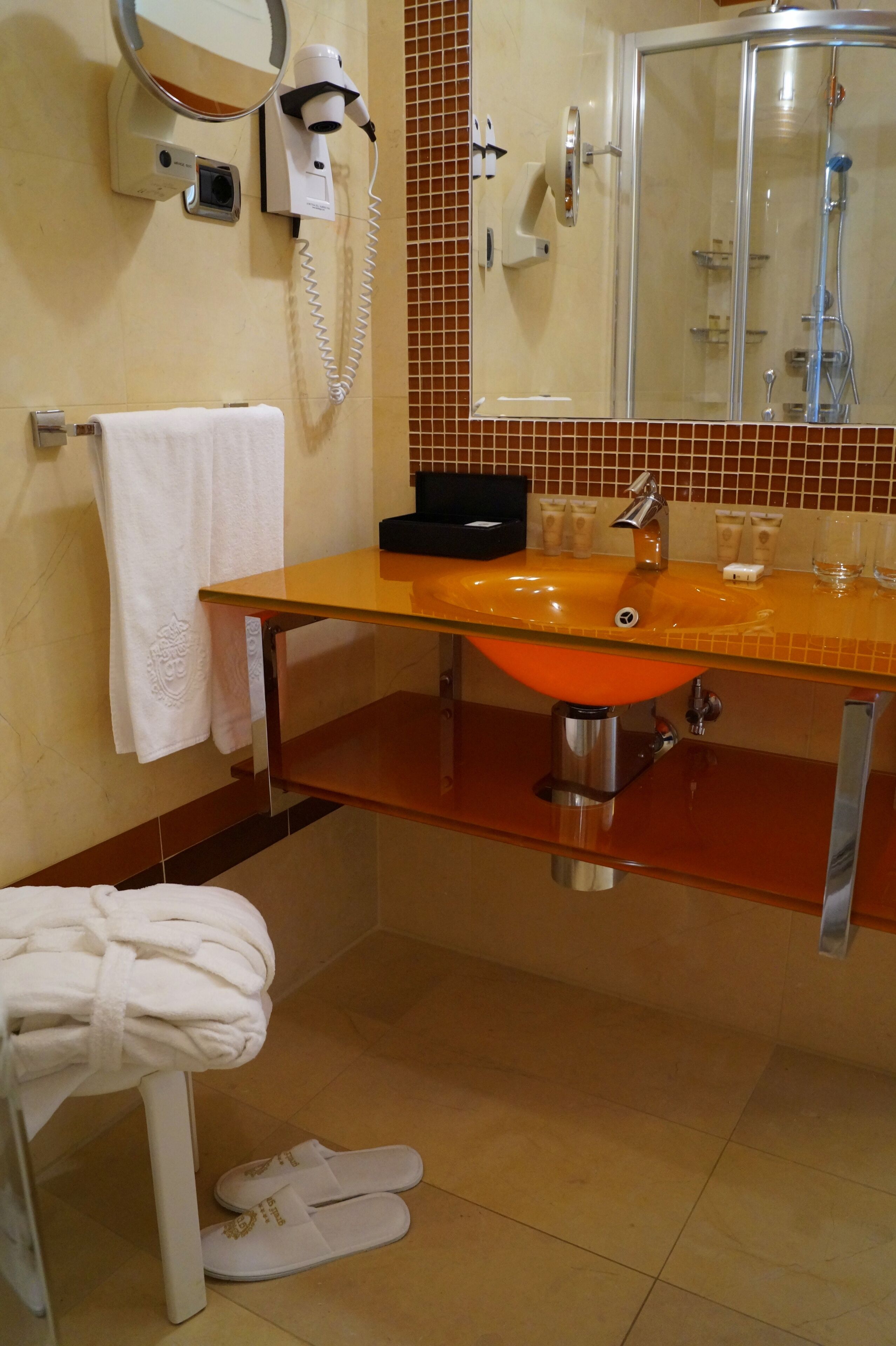 A bathroom with a glass shower enclosure, a sink with a mirror above it, and a towel rack with a white towel.