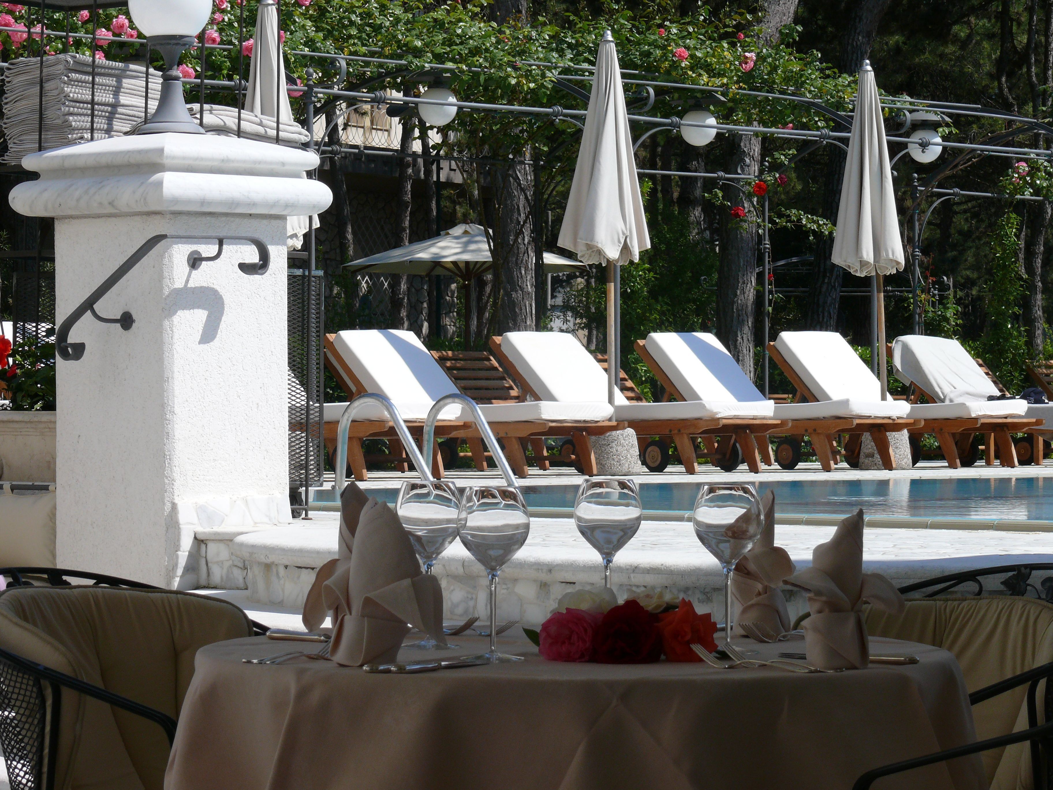 A poolside area with lounge chairs, a table set for dining, and umbrellas.