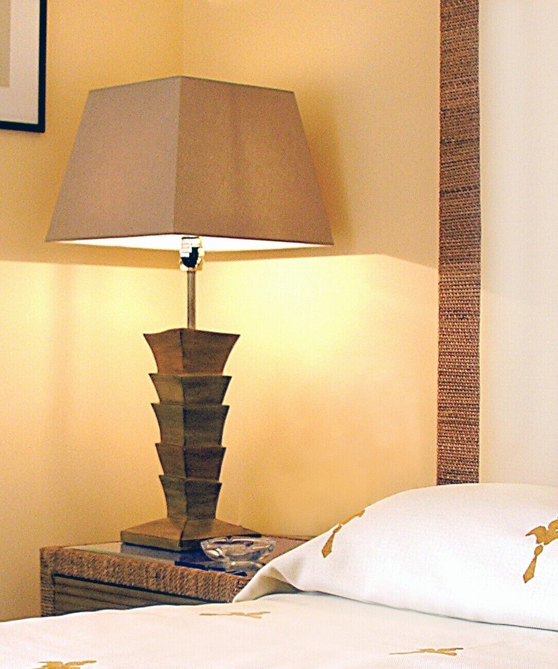 Una cama con un almohadón blanco y una lámpara en la mesita de noche.