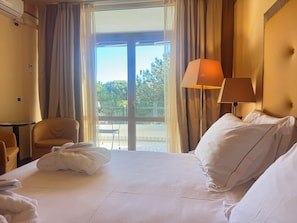A hotel room with a bed, a chair, a table, and a view of the outdoors. - Hotel Greif (Lignano Sabbiadoro)