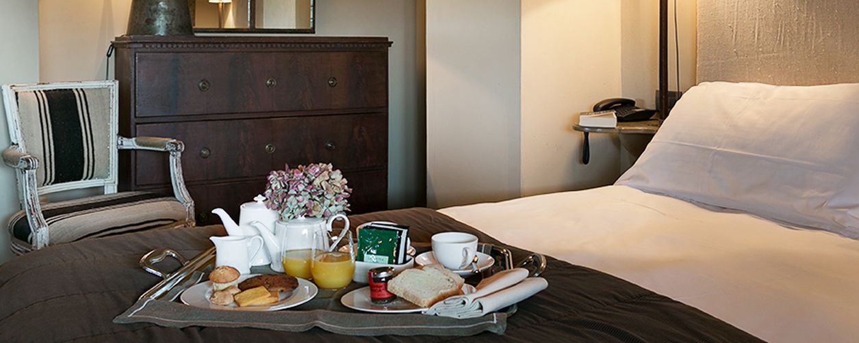 Una cama bien hecha con una bandeja de desayuno que incluye tostadas, huevos y jugo.