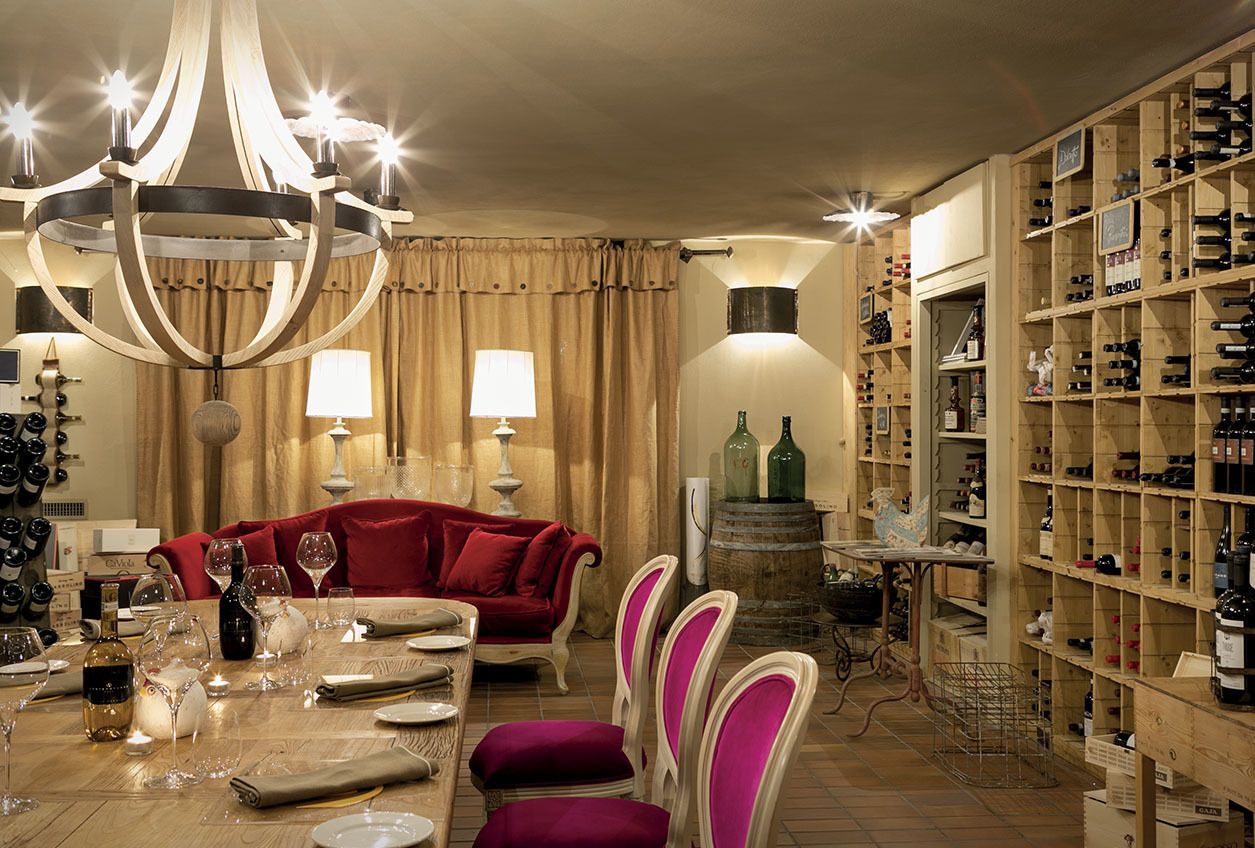 A dining area with a chandelier, red sofa, wooden dining table, and wine racks.