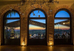 A restaurant with three arched windows overlooking a scenic landscape. - Albergo Ostelliere (Gavi)