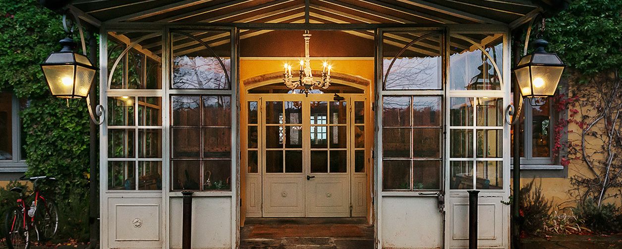 A covered entrance with a chandelier, large windows, and two wall-mounted lamps.