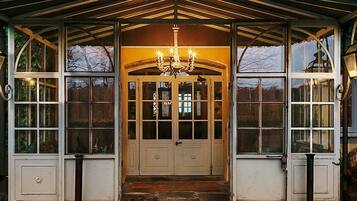 A covered entrance with a chandelier, large windows, and two wall-mounted lamps.