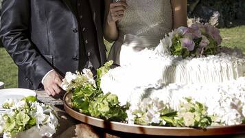 A wedding cake with white frosting and floral decorations, surrounded by guests.