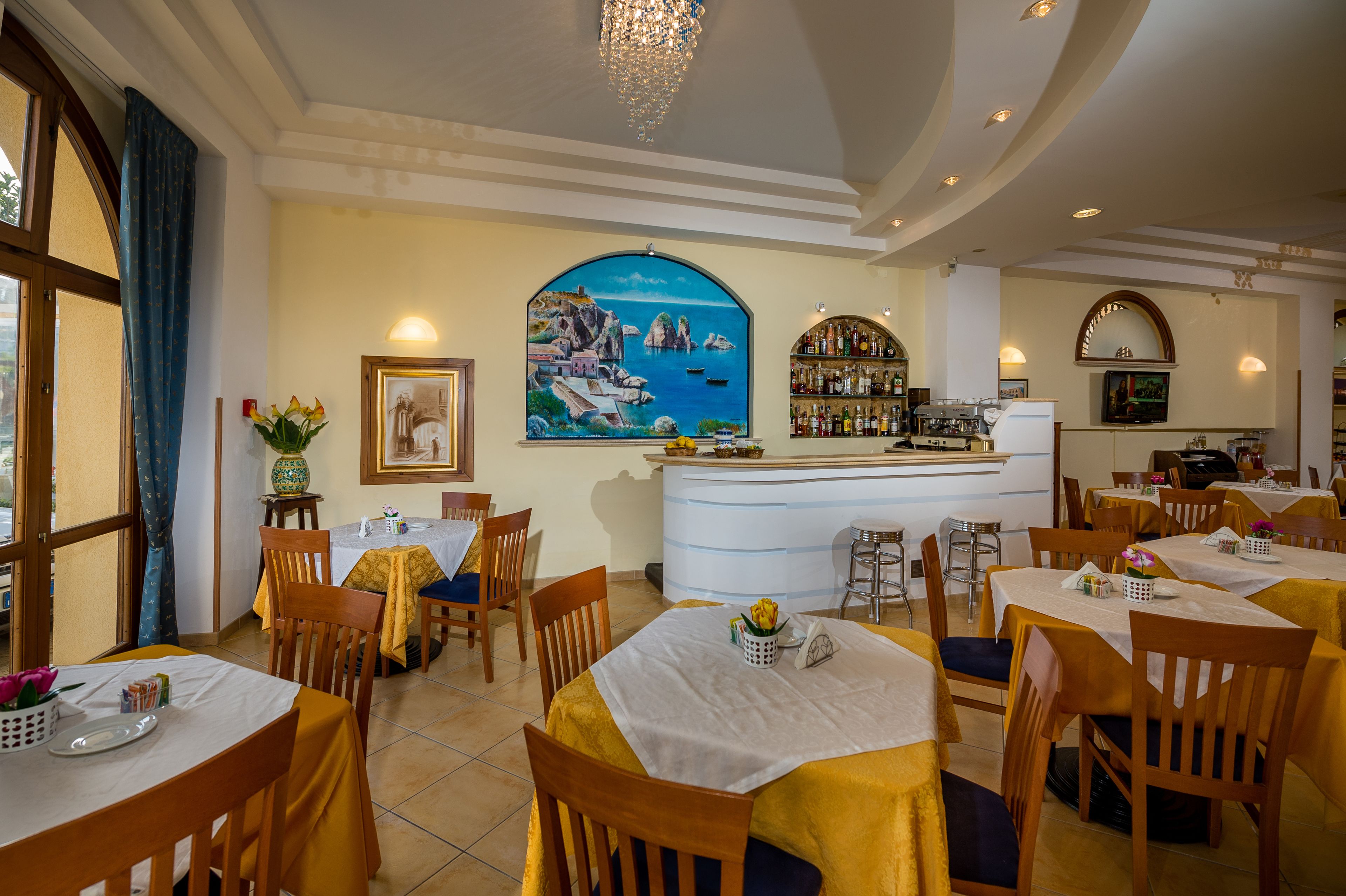 Un restaurante con varias mesas, sillas, una zona de bar y un mural en la pared.