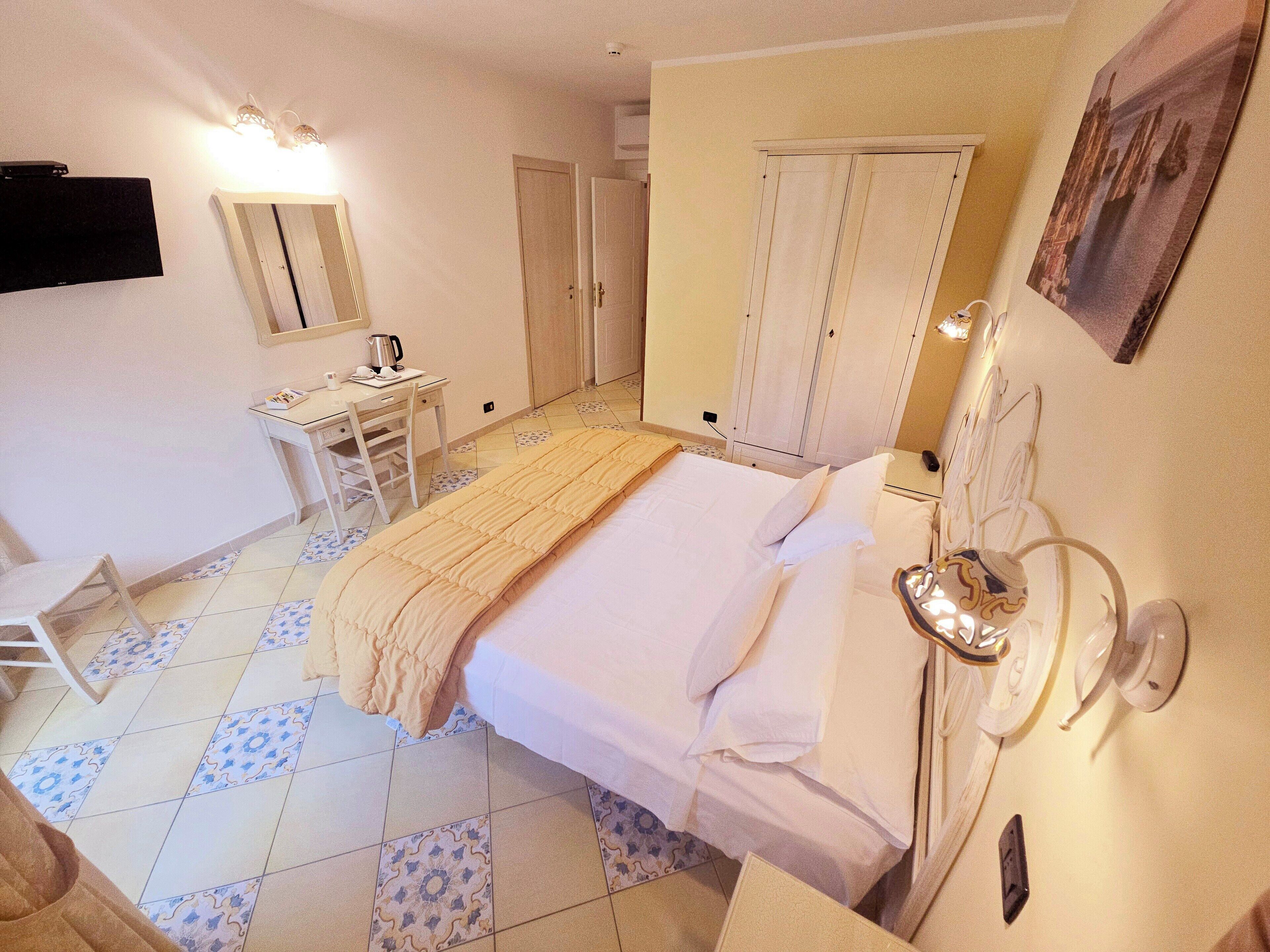 Una habitación de hotel con cama, mesita de noche, lámpara, armario y escritorio con silla.