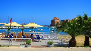 Un port de plaisance avec des bateaux, un café doté d’une terrasse, et un bâtiment historique en arrière-plan.