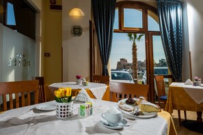 Ein Hotel-Speisesaal mit gedeckten Tischen für das Frühstück und Blick auf die Stadt durch große Fenster.