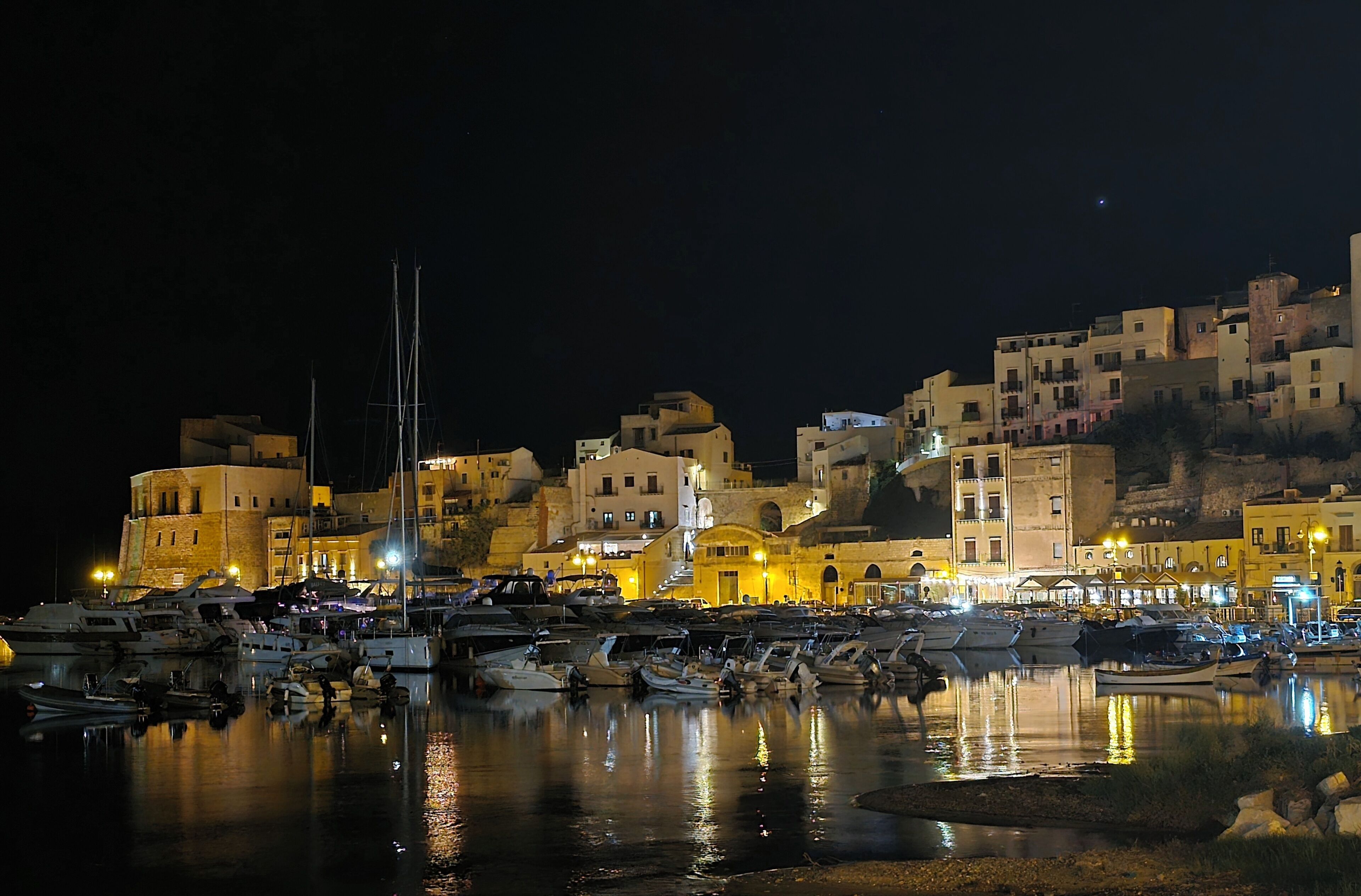 Un port de plaisance avec des bateaux amarrés, des bâtiments dotés de balcons et une colline en arrière-plan.