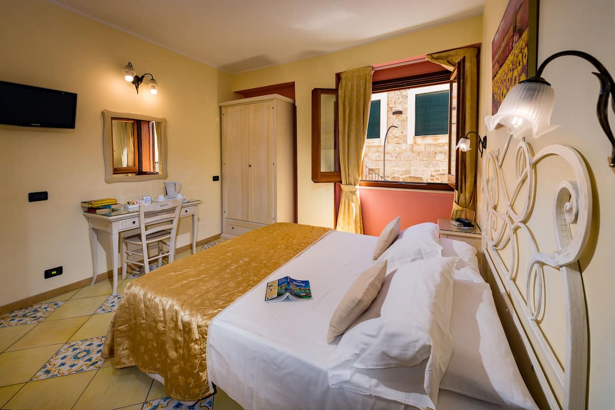 Ein Hotelzimmer mit Bett, Schreibtisch, Stuhl, Fernseher und einem Fenster mit Vorhängen.