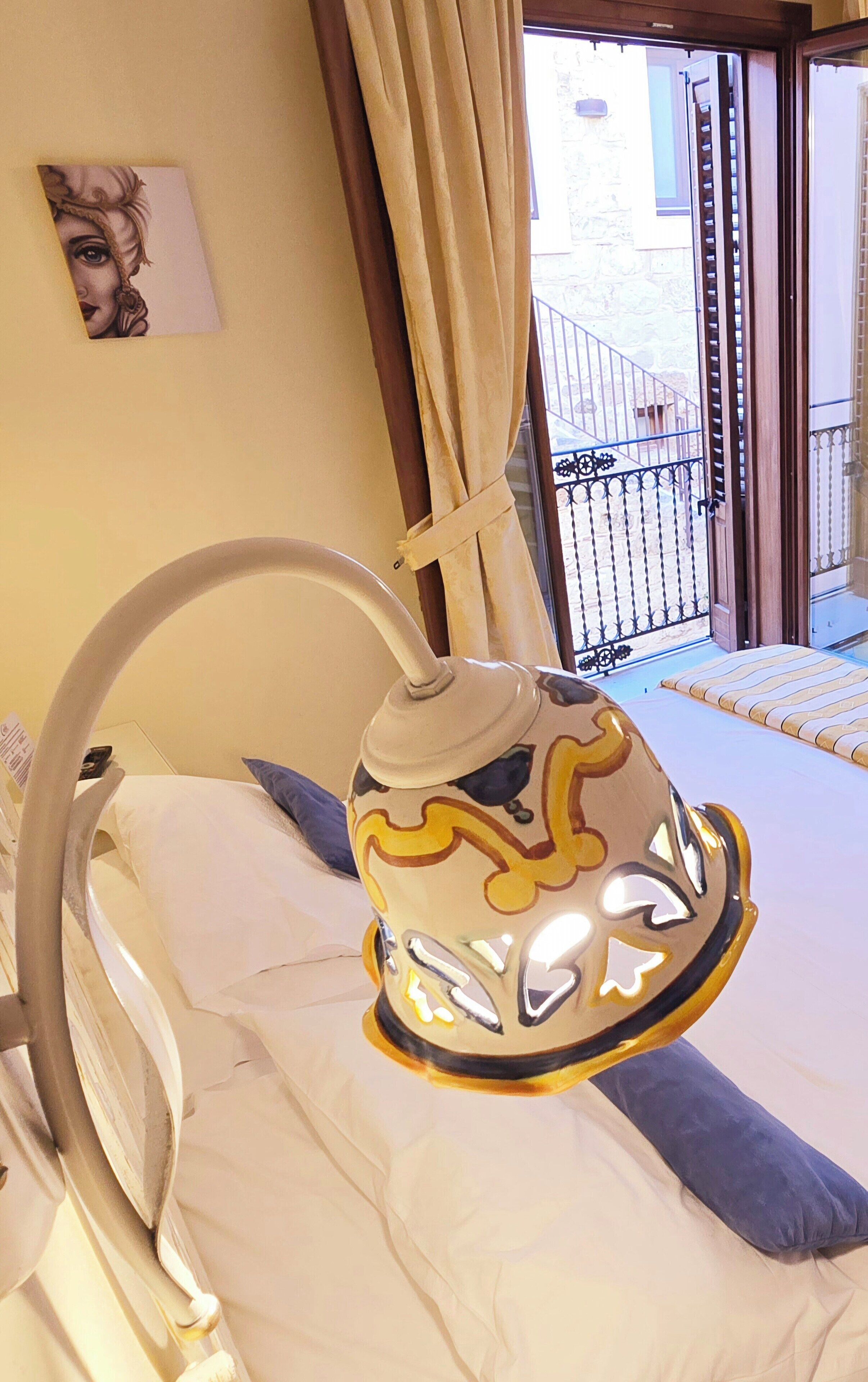 A bed with a decorative lamp, a pillow, and a window with curtains.