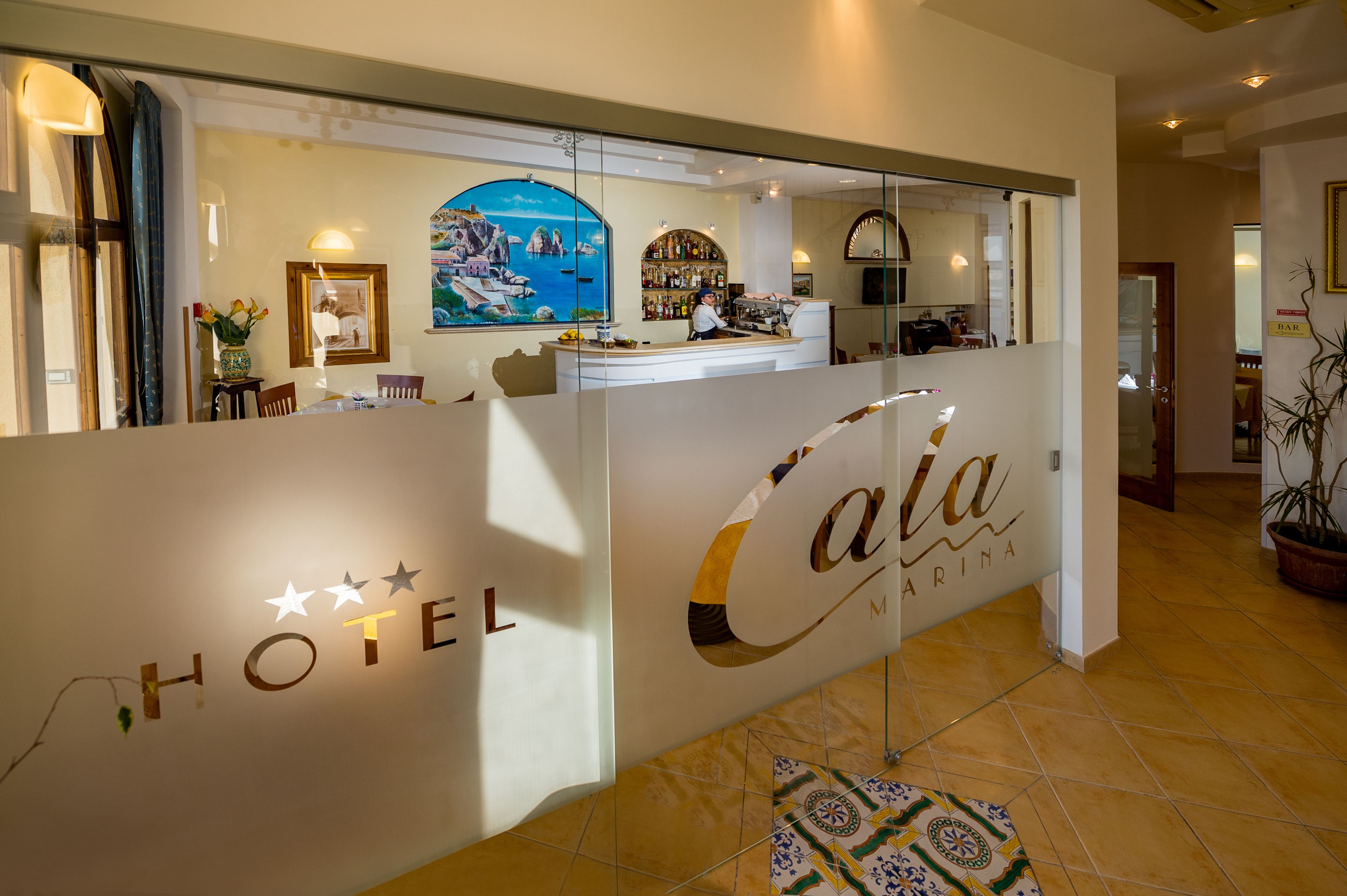 Un espace d’accueil d’hôtel comprenant un comptoir, un bar et un tableau représentant un paysage côtier.