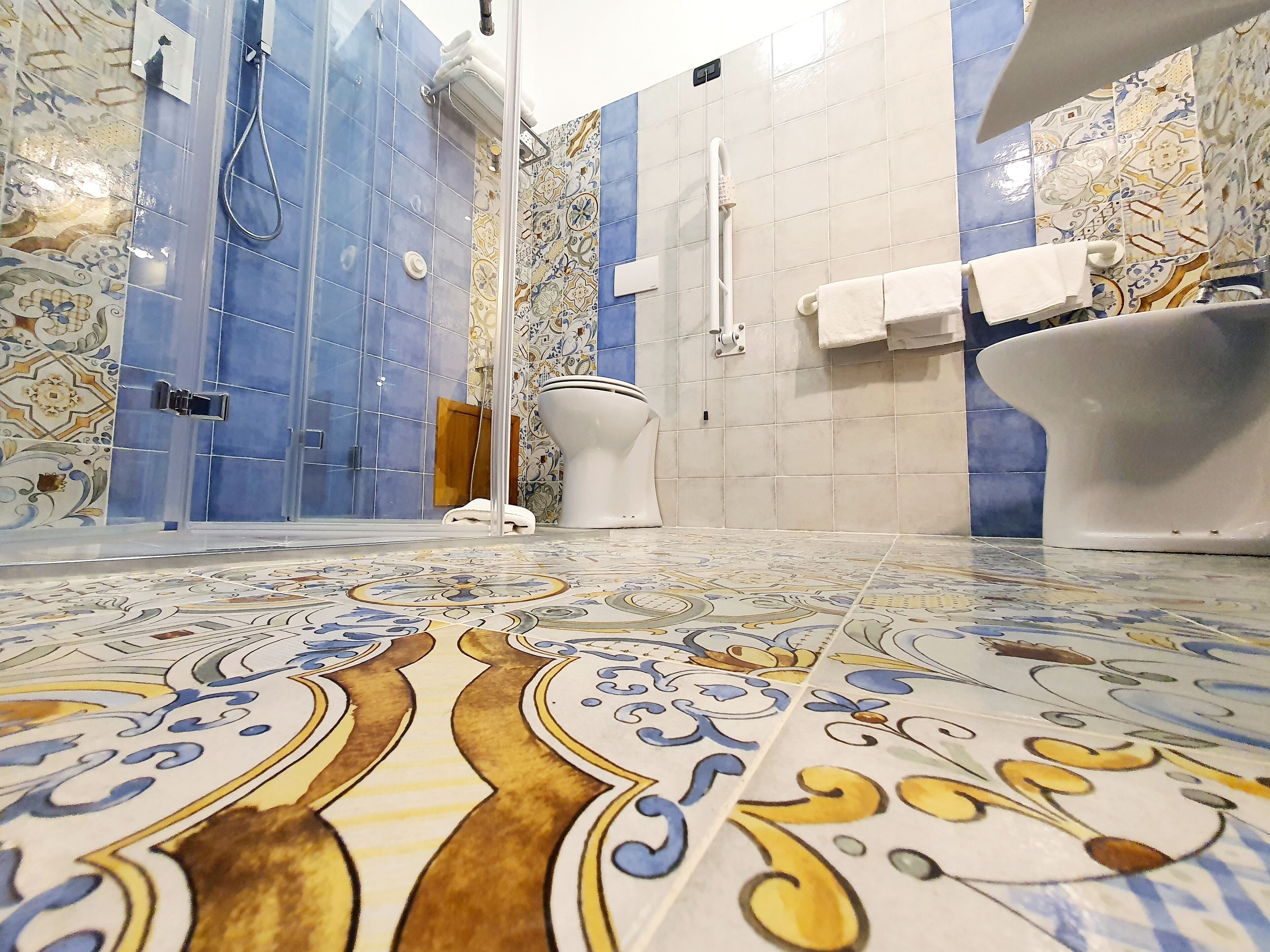 A bathroom with a shower, toilet, and bathtub, featuring patterned tiles and a tiled floor.