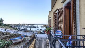 A balcony overlooking a marina with boats, a stone pathway, and a parked car.