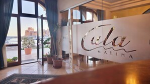 Un hall d’hôtel avec une grande porte vitrée, des plantes en pot et une enseigne indiquant « Cala Madina ».