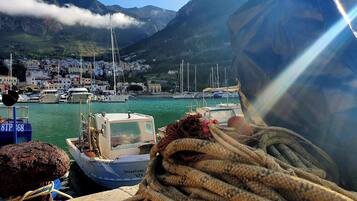 Un puerto con barcos, una montaña rocosa al fondo y un pueblo con edificios.