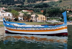 Un bote colorido amarrado cerca de un muelle con edificios y vegetación al fondo.