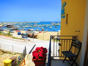 Ein Balkon mit Blick auf einen Hafen voller Boote, einer Bank und einem Blumentopf mit roten Blüten.