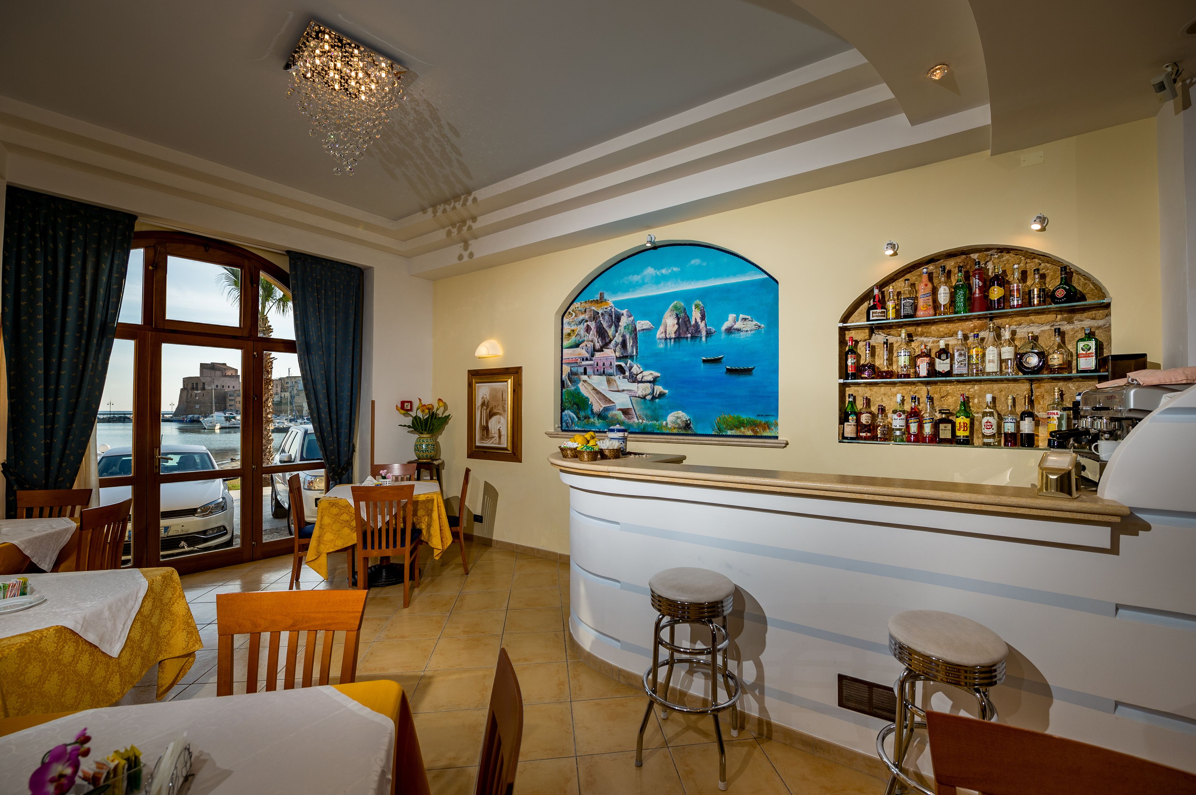 A restaurant with a bar, dining tables, chairs, and a view of the sea through a large window.