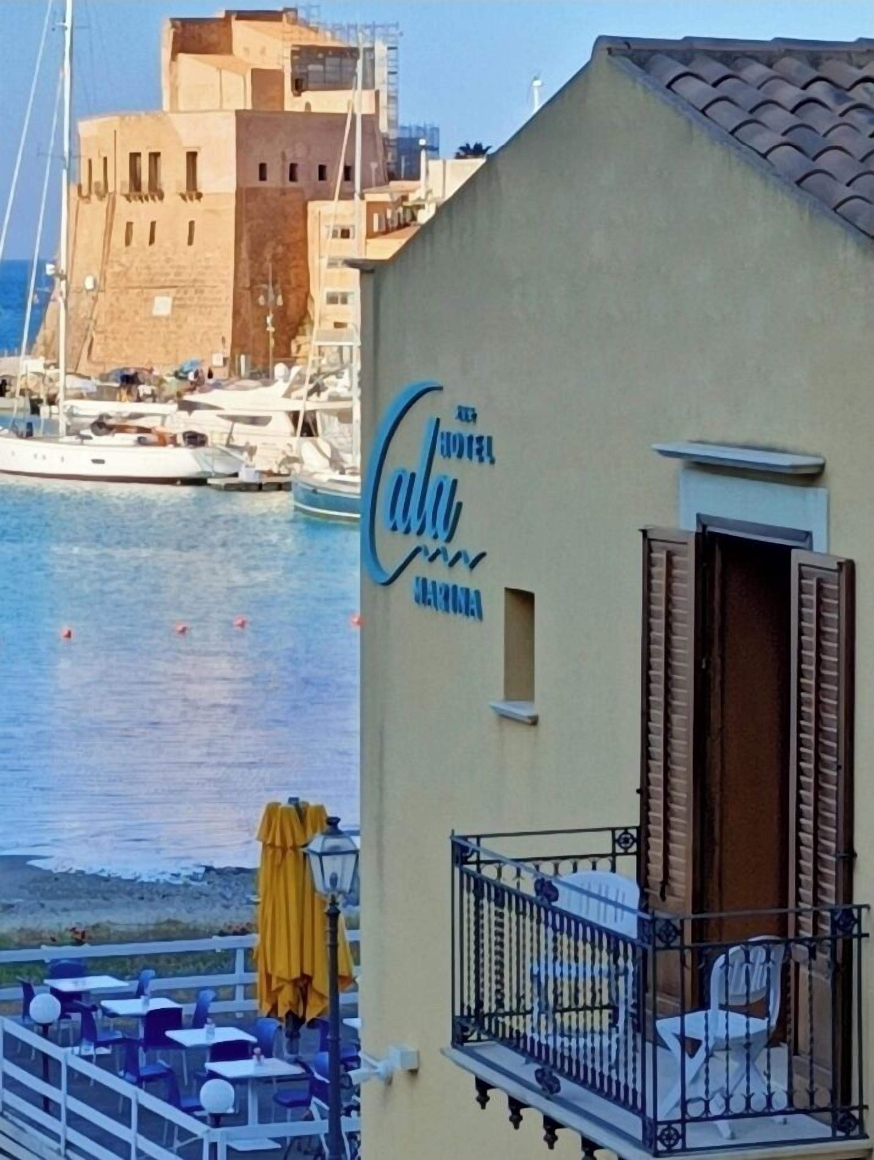 Un hotel frente al mar con balcón, vista al océano y barcos al fondo.