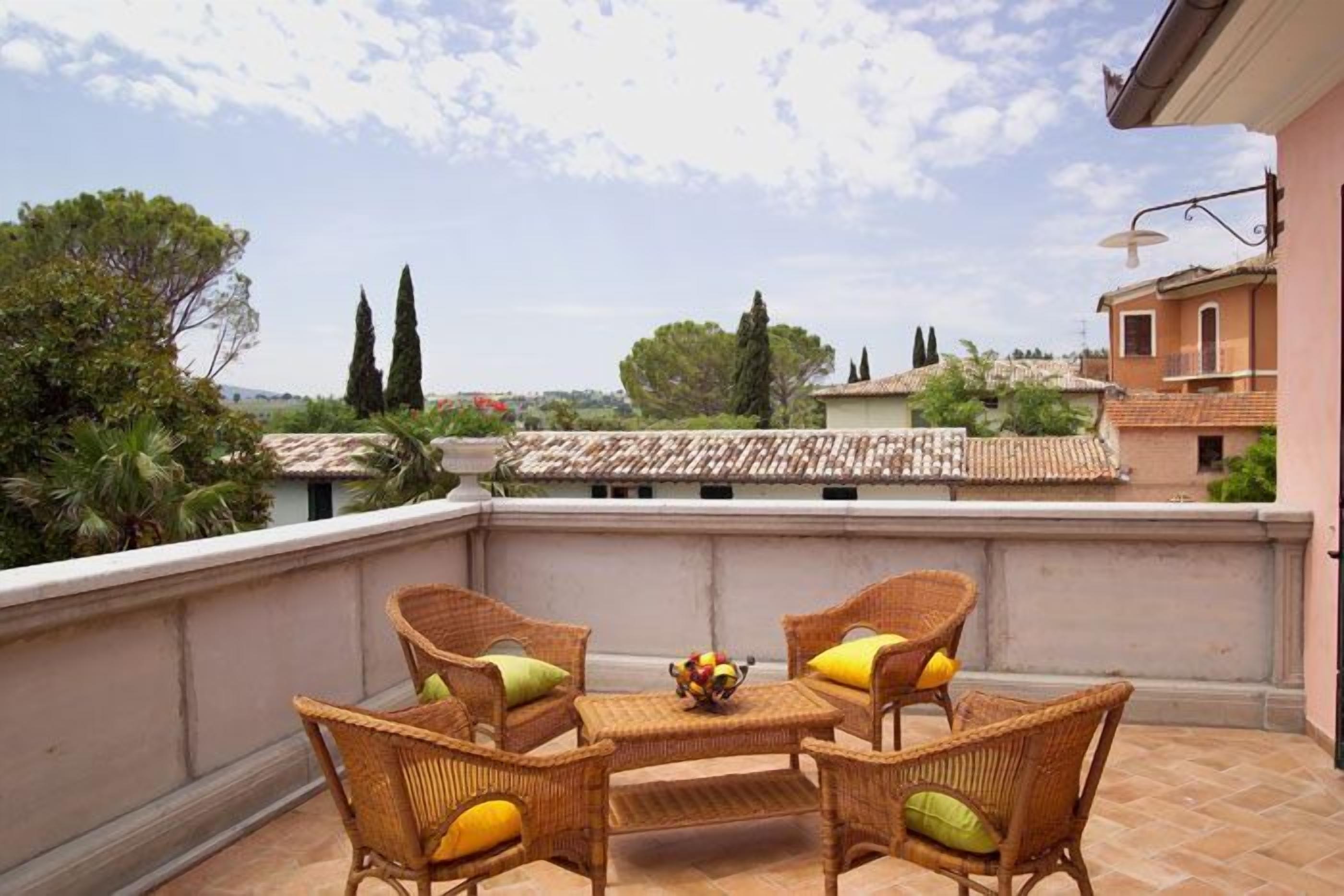 A terrace with wicker furniture and a fruit bowl, overlooking a residential area with trees and buildings.