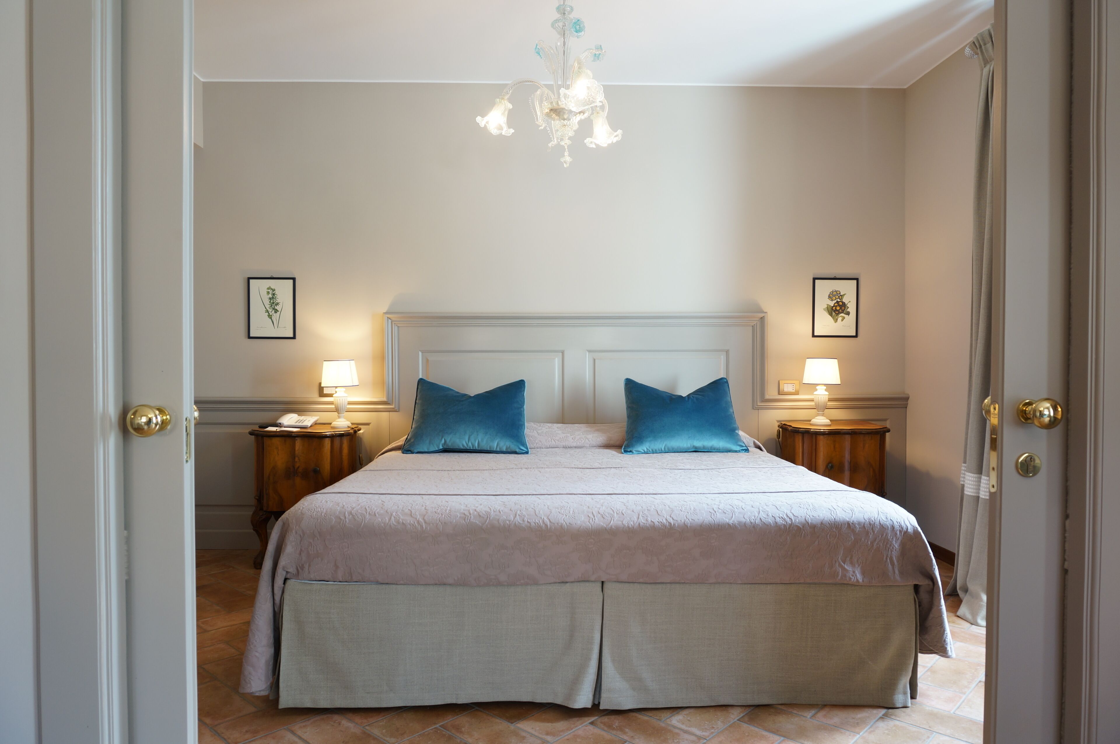Una camera da letto con un letto grande, due lampade ai comodini, un lampadario e quadri appesi alle pareti.