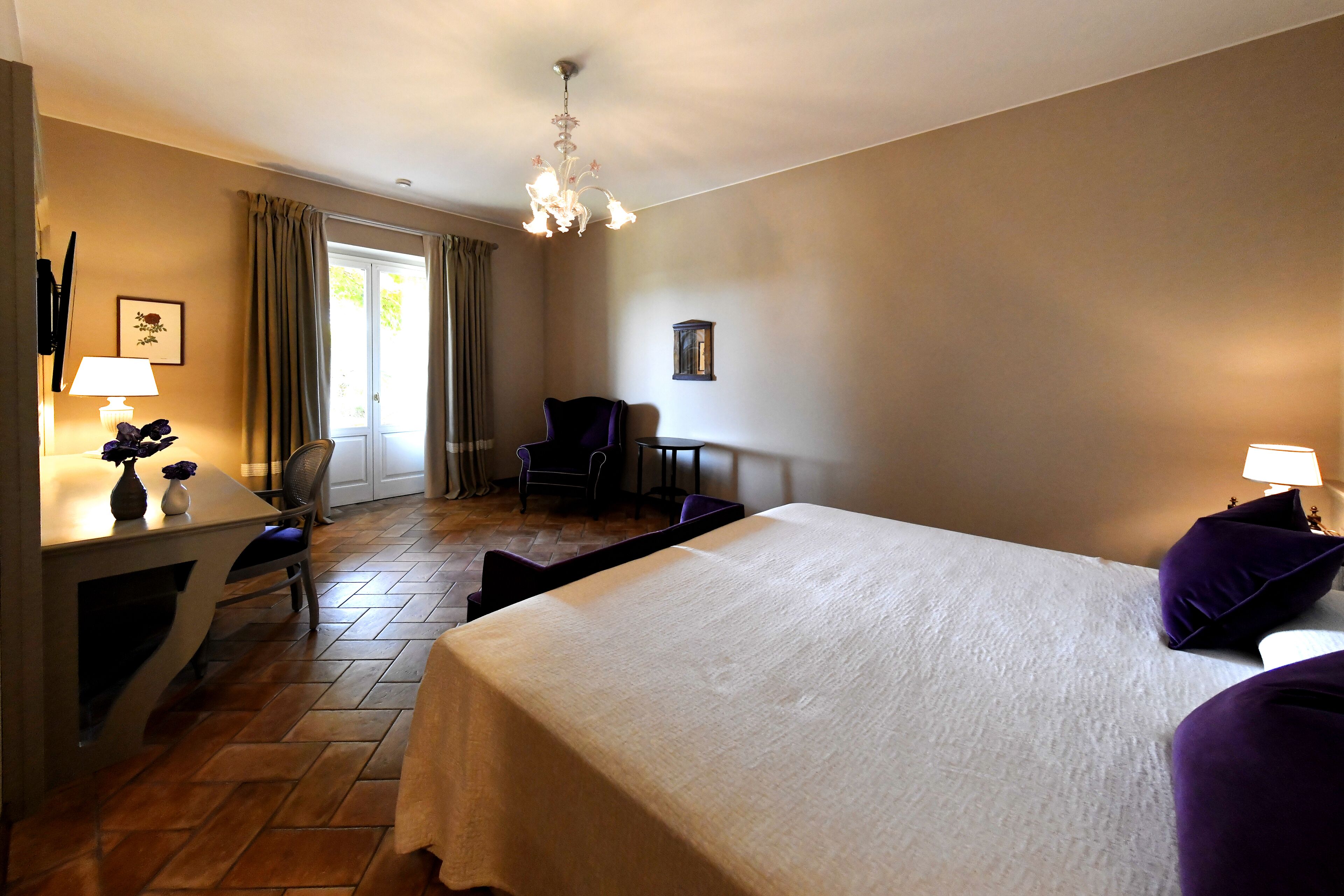Una camera d'albergo con un letto, una scrivania, una sedia, un tavolino e una finestra con tende.