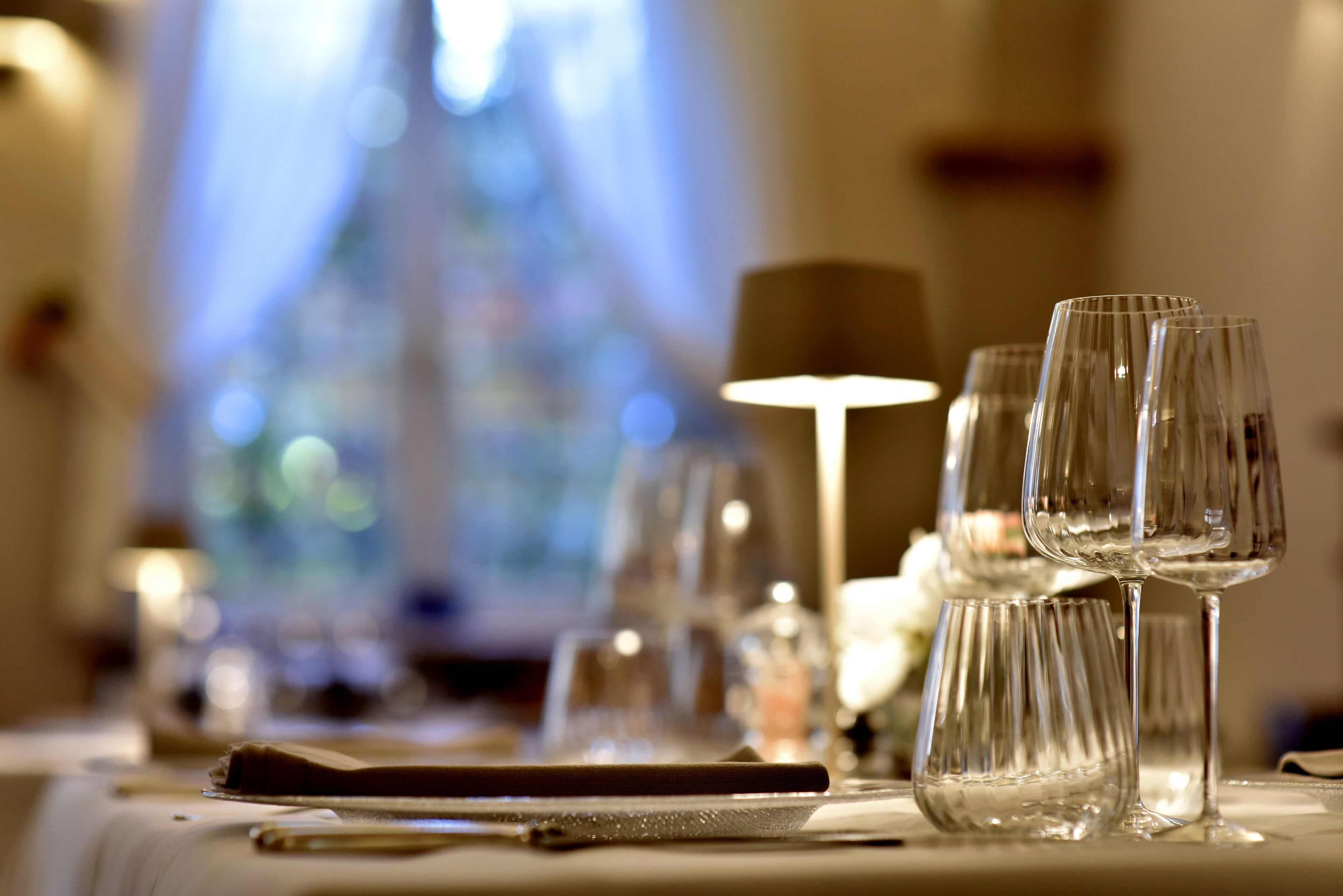 A dining table with wine glasses and cutlery, a candle, and a lamp.