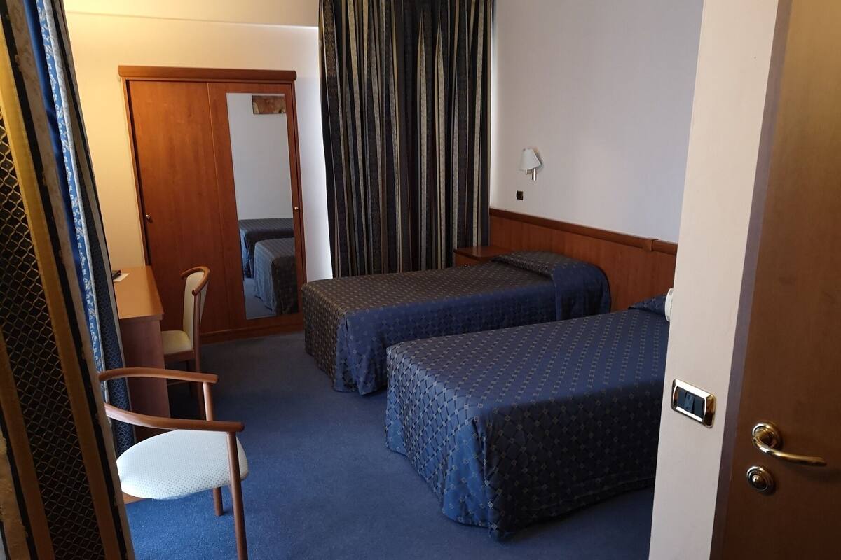 A hotel room with two beds, a chair, a desk, and a mirror.