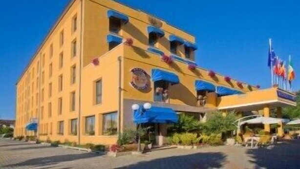 A multi-story hotel with balconies, a central entrance, and flags.