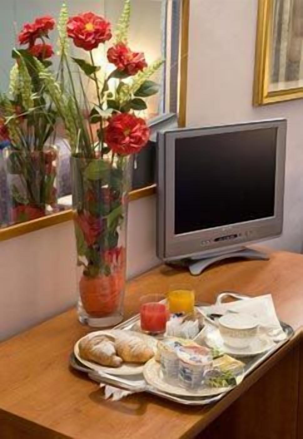 A hotel room with a breakfast tray, a television, and a vase with red flowers.