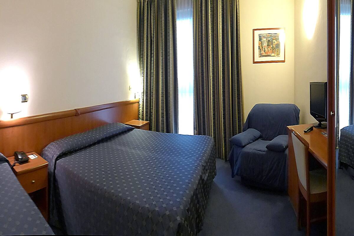 A hotel room with two single beds, a desk with a chair, a television, and a painting on the wall.