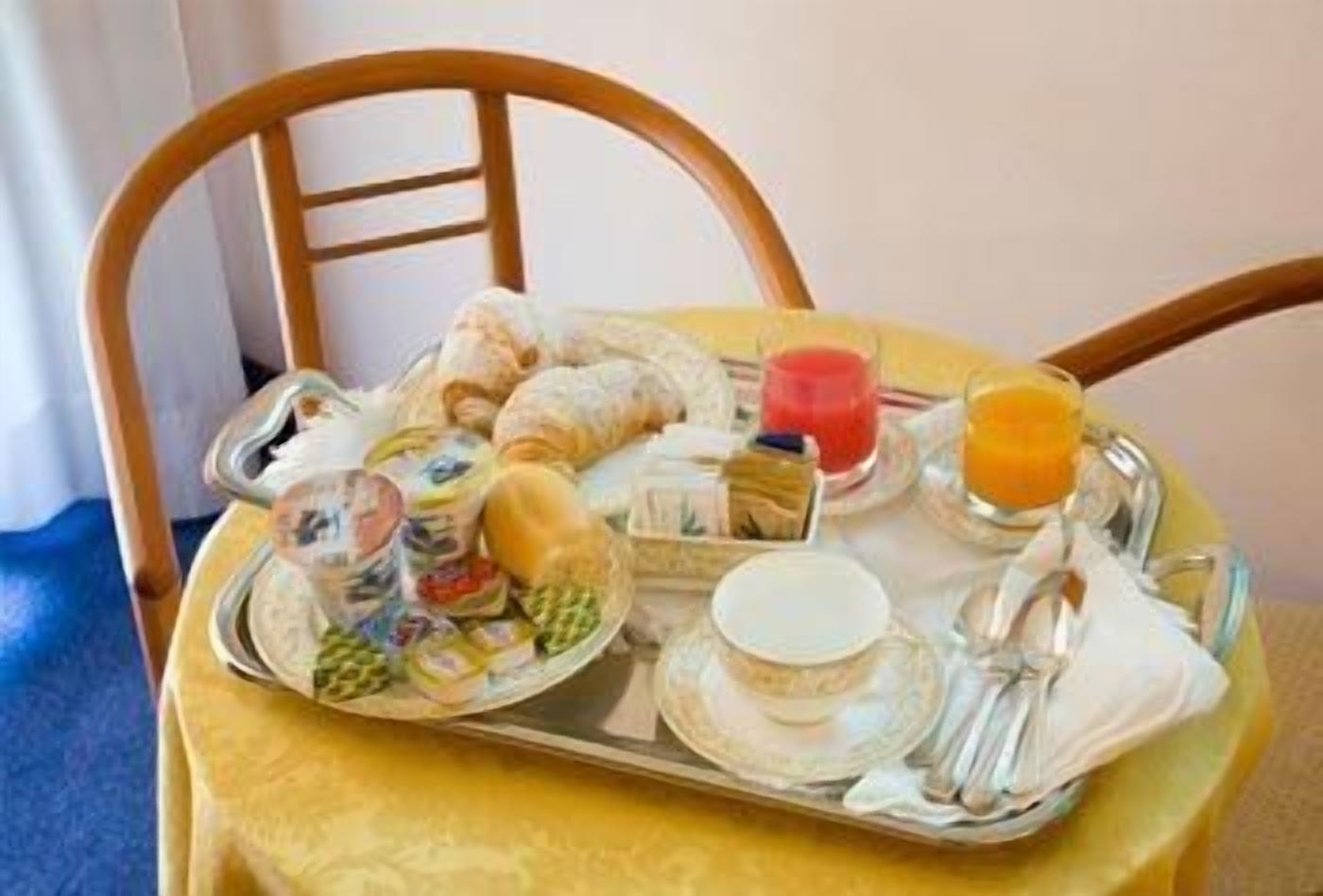 Uma bandeja de café da manhã com croissants, uma tábua de frutas, suco e uma xícara de café sobre uma mesa com toalha amarela.