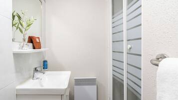 Ein Badezimmer mit weißem Waschbecken, einem Spiegel, einer Pflanze, einem Handtuch und einer Dusche mit Glastür.