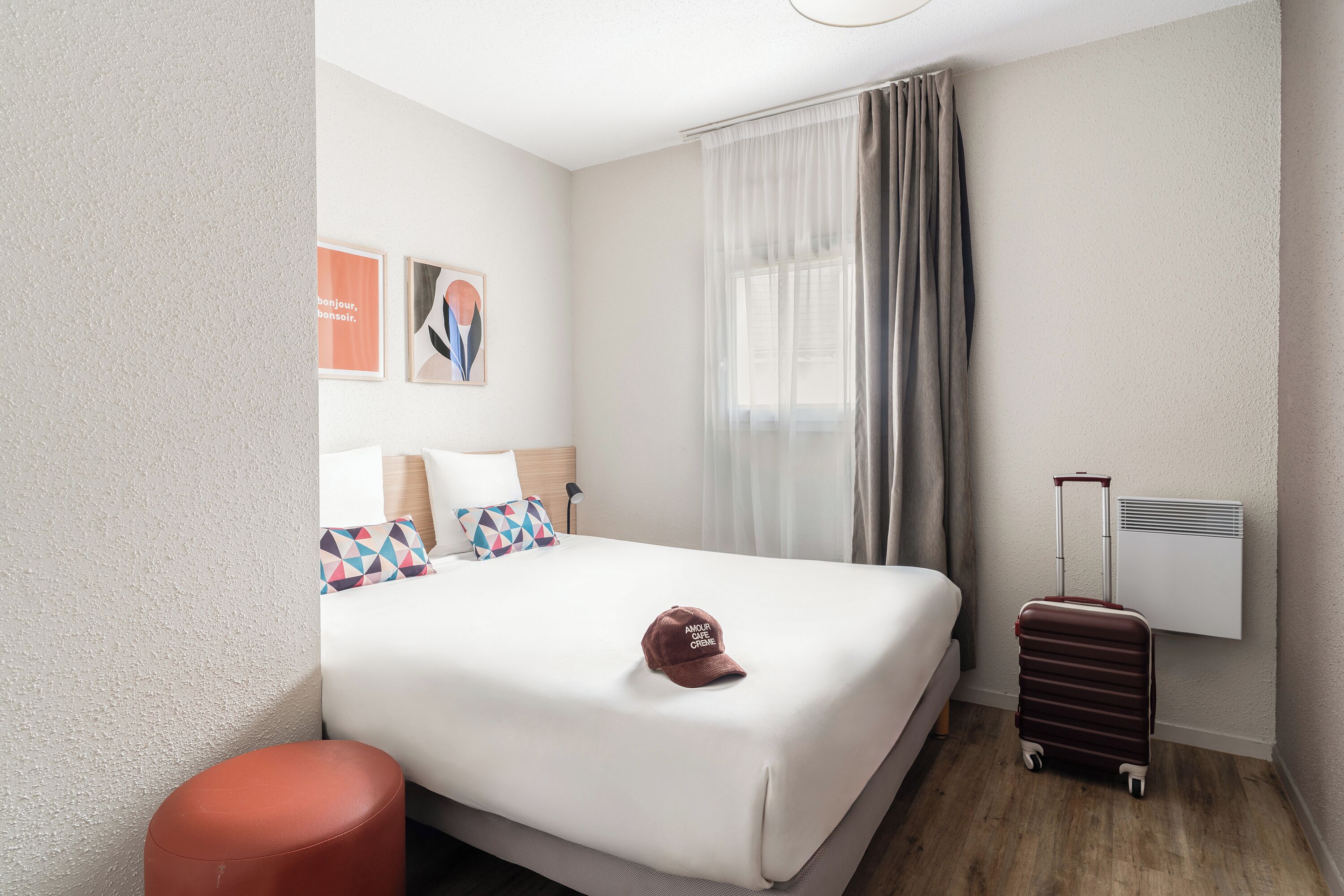 Quarto de hotel com cama, mala, abajur e ar-condicionado fixado na parede.