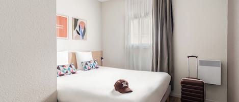 Une chambre d’hôtel avec un lit, une valise, une lampe et un climatiseur fixé au mur.