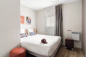 Habitación de hotel con cama, maleta, lámpara y aire acondicionado instalado en la pared.